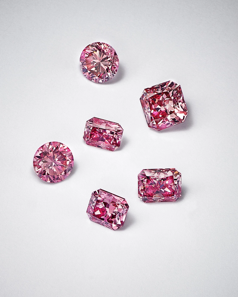 Six pink diamonds are arranged on a white surface.